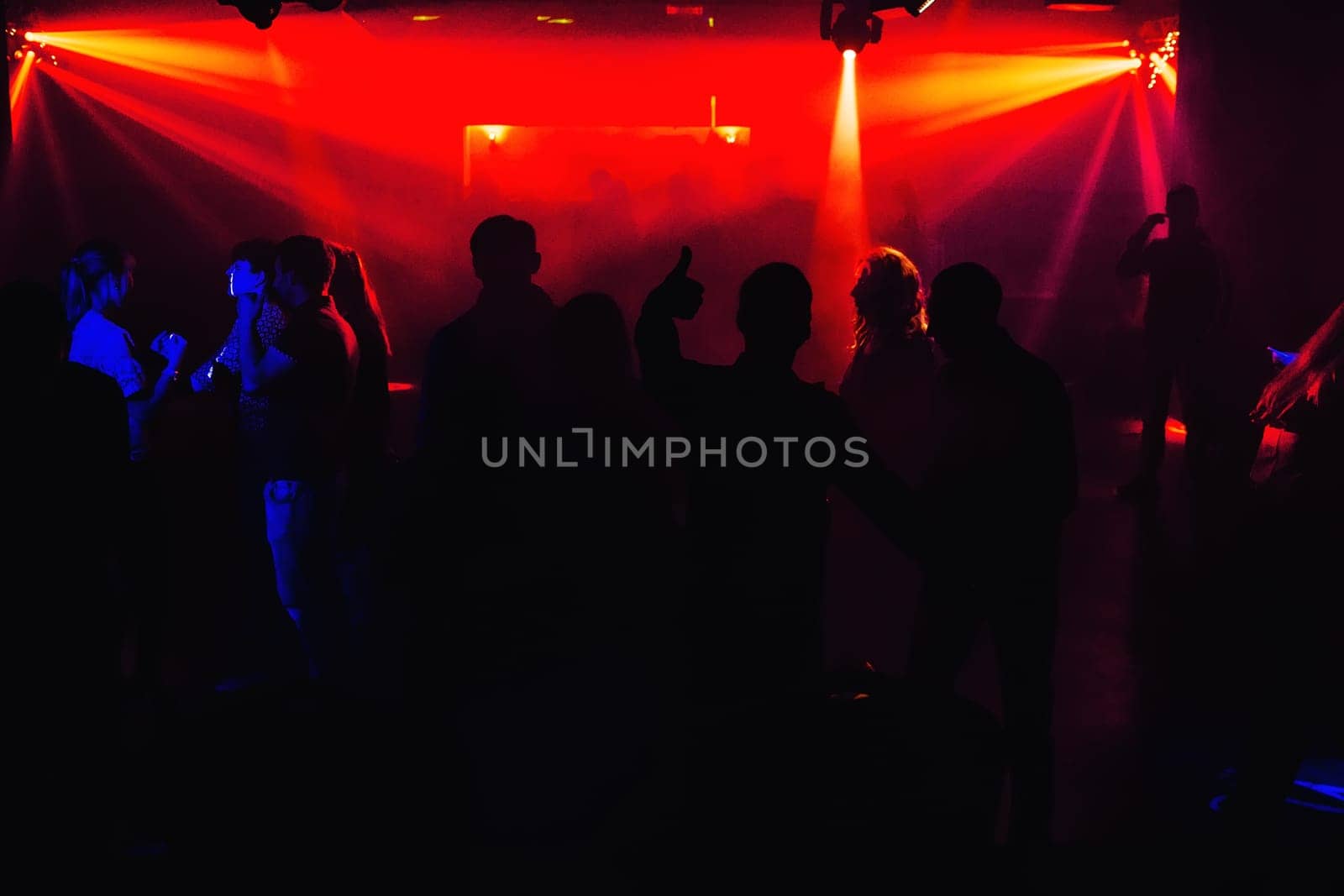 people silhouettes on the dance floor of a night club at the concert under red spotlights