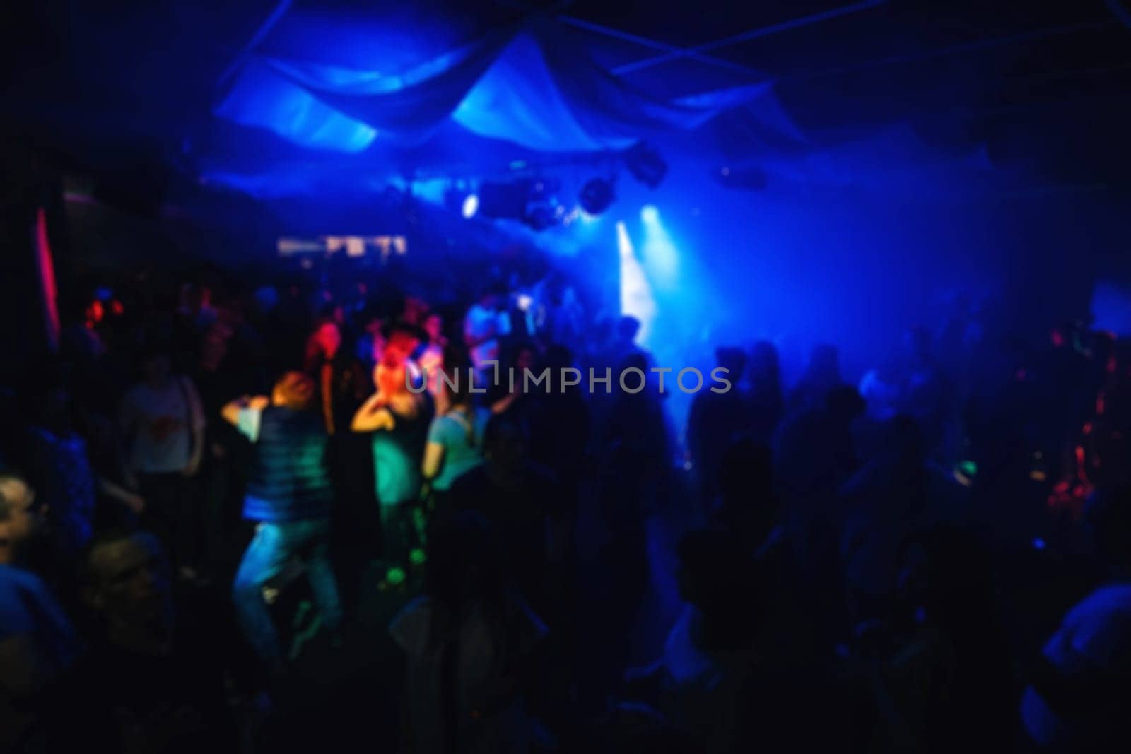 blurred silhouettes of people on the dance floor of a night club at the concert with a dark background and a glow of spotlights