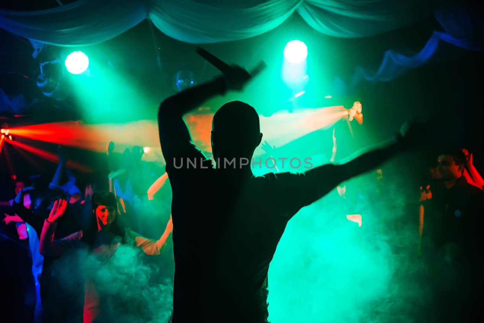blurred silhouette of the MC with a microphone on stage of nightclub