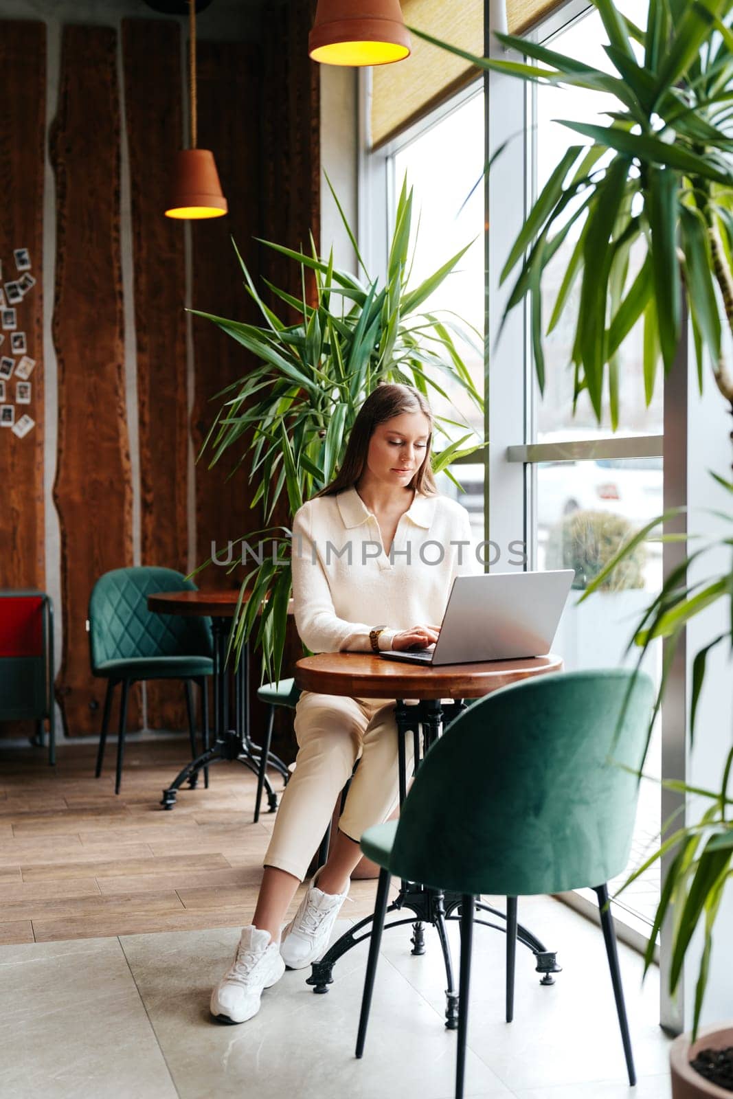 A woman of Indian descent is sitting at a wooden table, concentrating on her laptop screen. She appears to be working or studying intently, with a cup of coffee beside her. The room is well-lit and clutter-free.