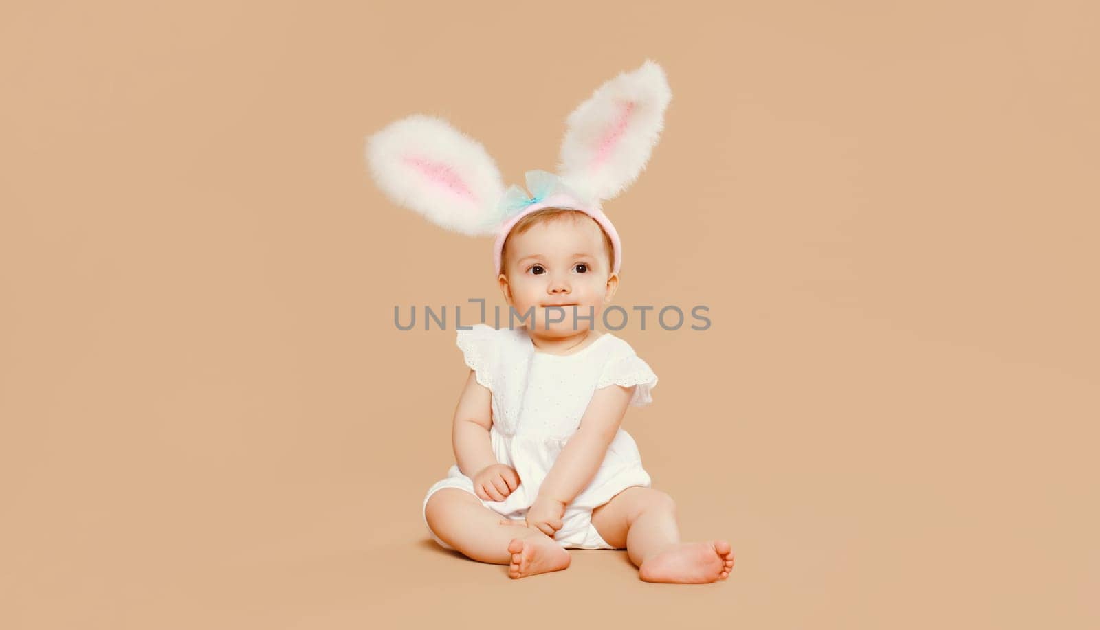 Portrait cute baby with easter rabbit ears sitting on brown studio background by Rohappy