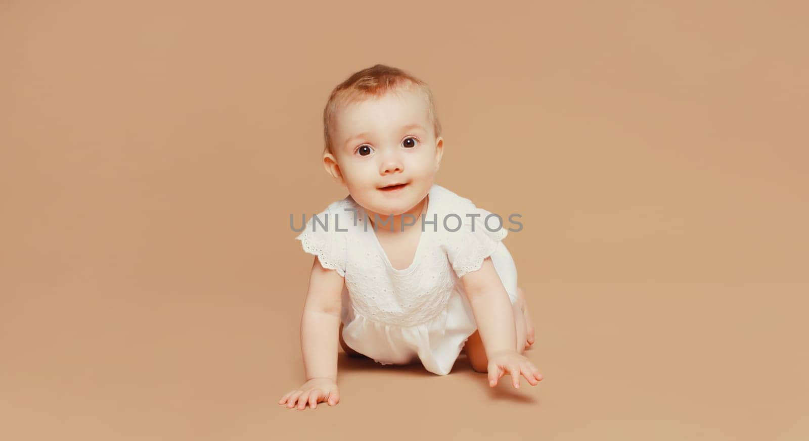 Happy cute baby crawling on the floor on brown studio background by Rohappy