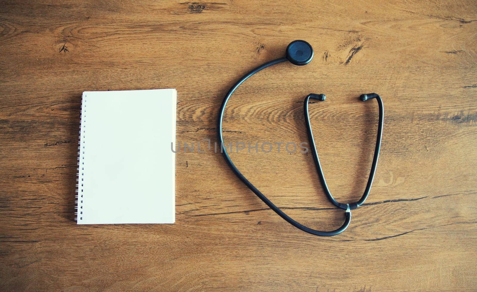 Medical stethoscope and white blank notebook for copy space text on wooden table, top view