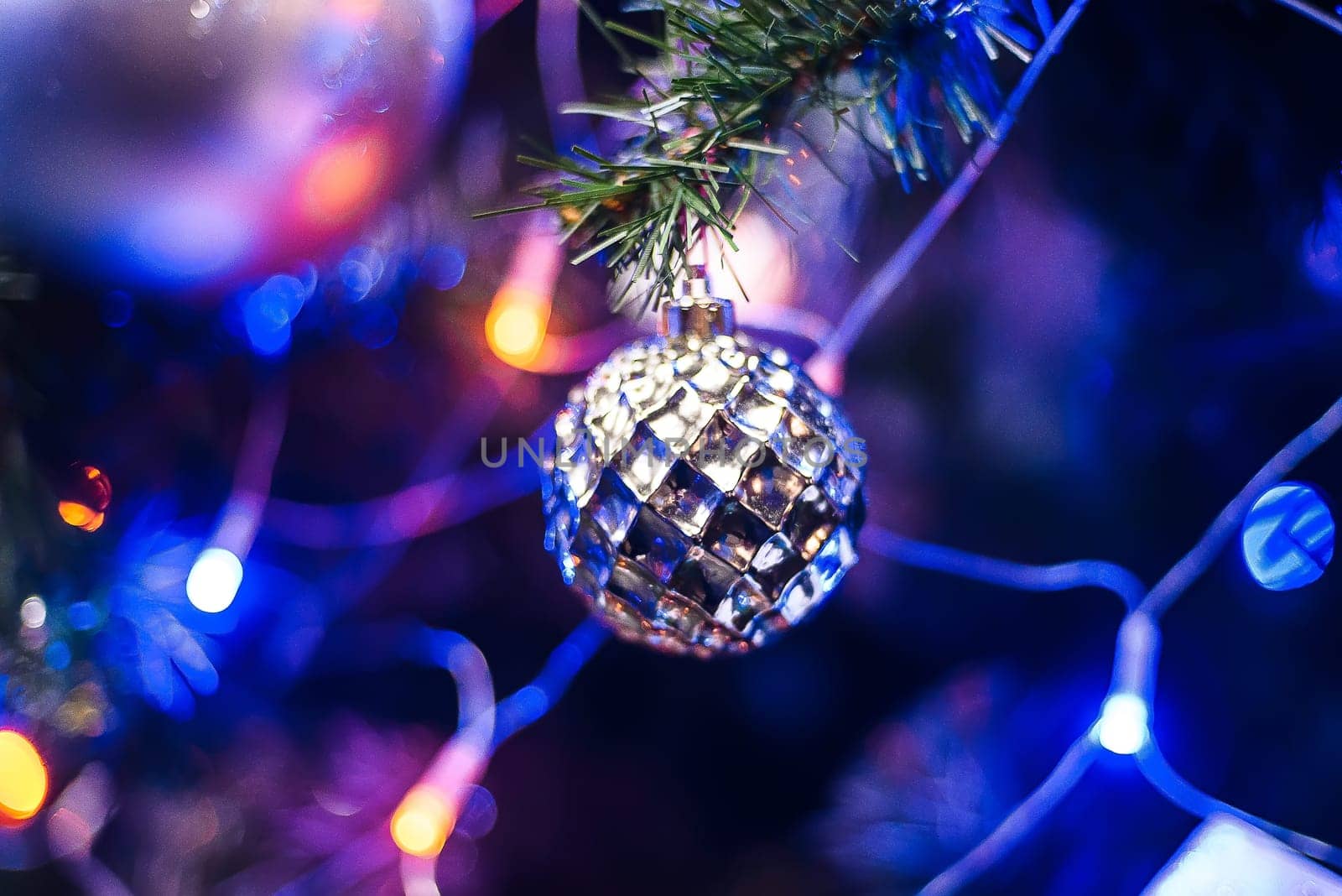 ball toy on branch of Christmas tree for new year with blurred colorful background of lights garland fortraditional new year