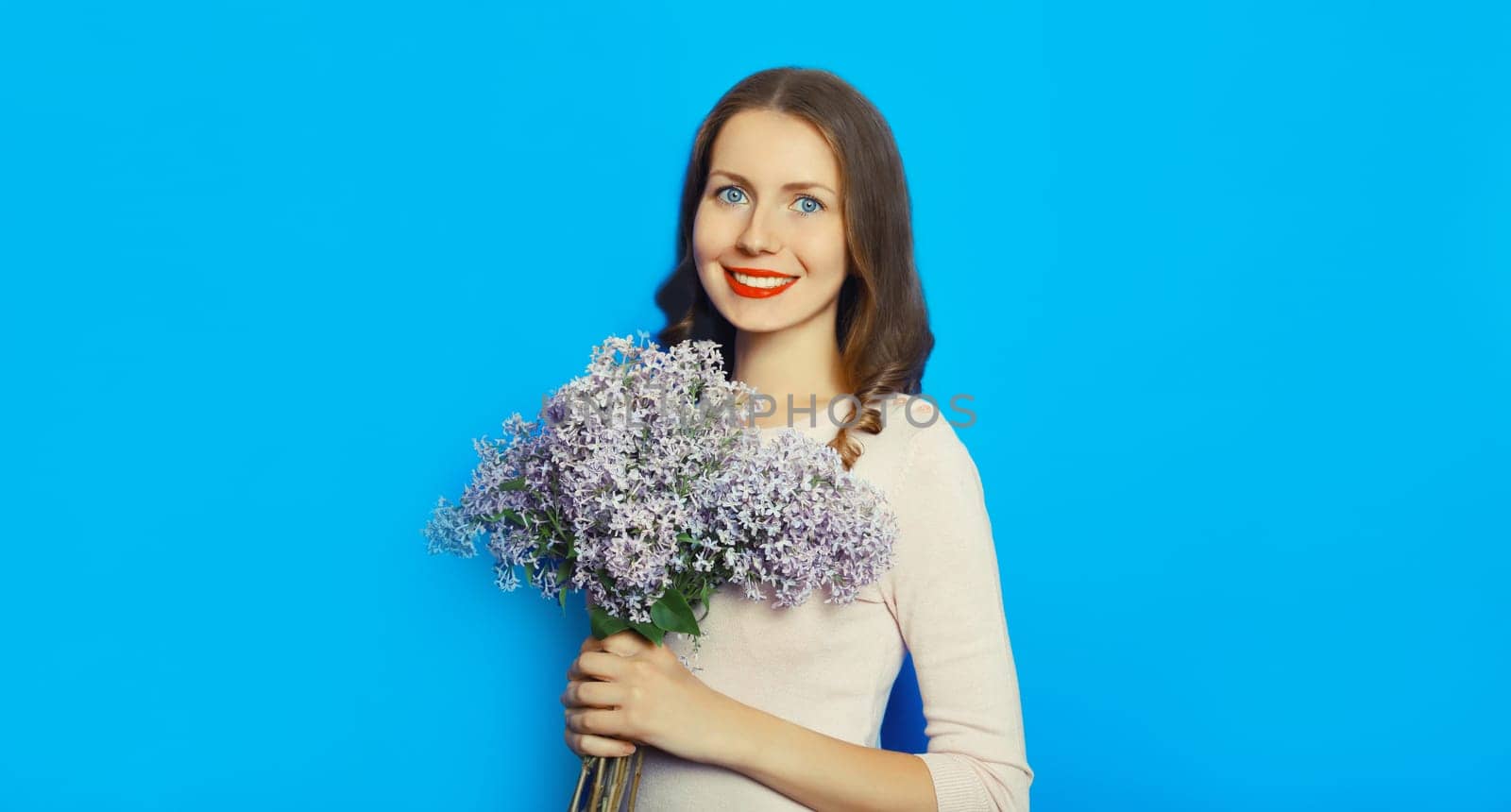 Portrait of beautiful happy smiling woman with bouquet of fresh lilac flowers, wildflowers on blue background