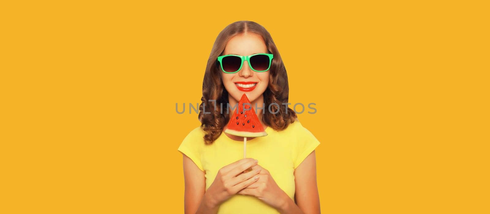 Summer portrait of happy young woman with fresh juicy fruits, lollipop or ice cream shaped slice of watermelon on yellow studio background