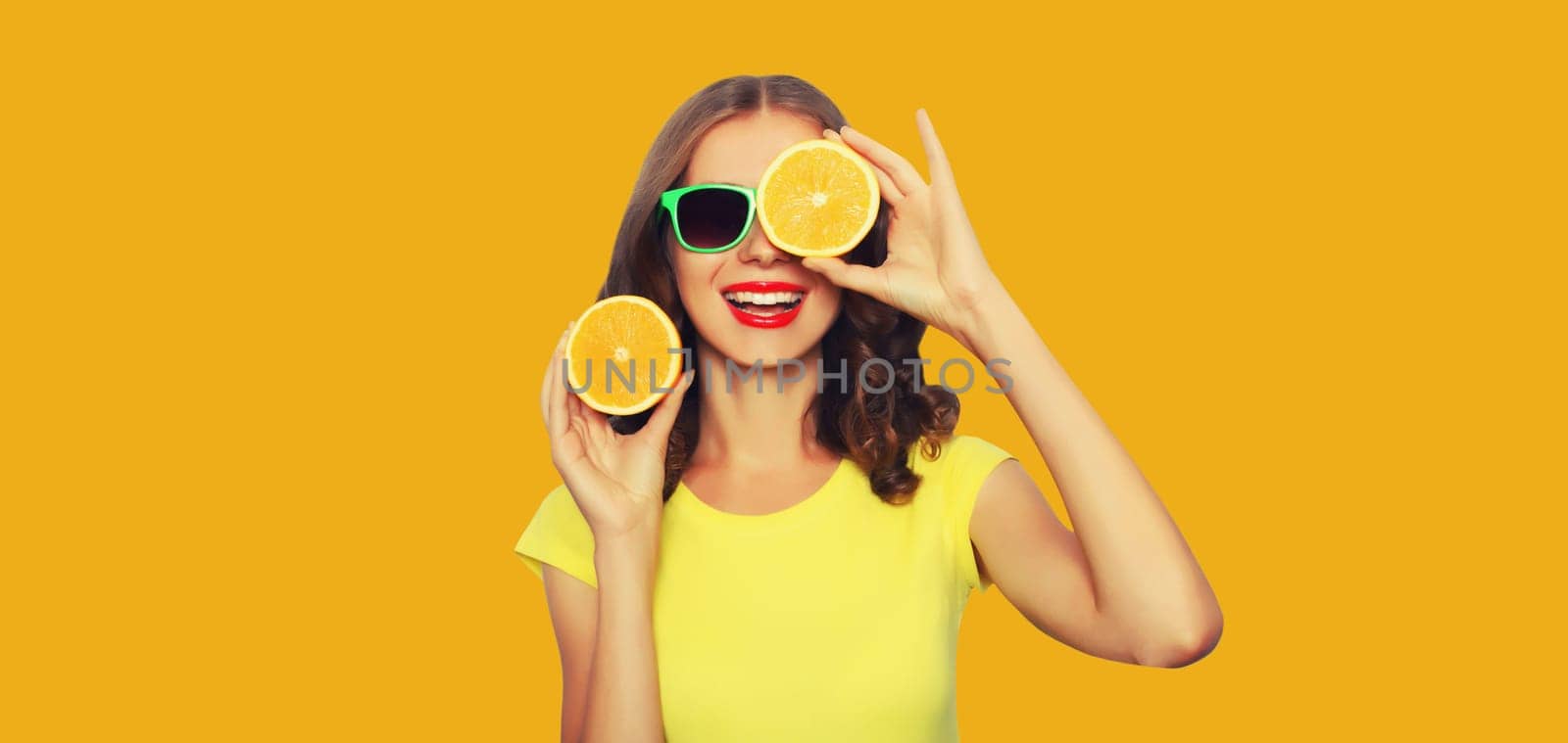 Summer vacation portrait of happy smiling young woman with fresh juicy fruits, slice of orange on yellow studio background