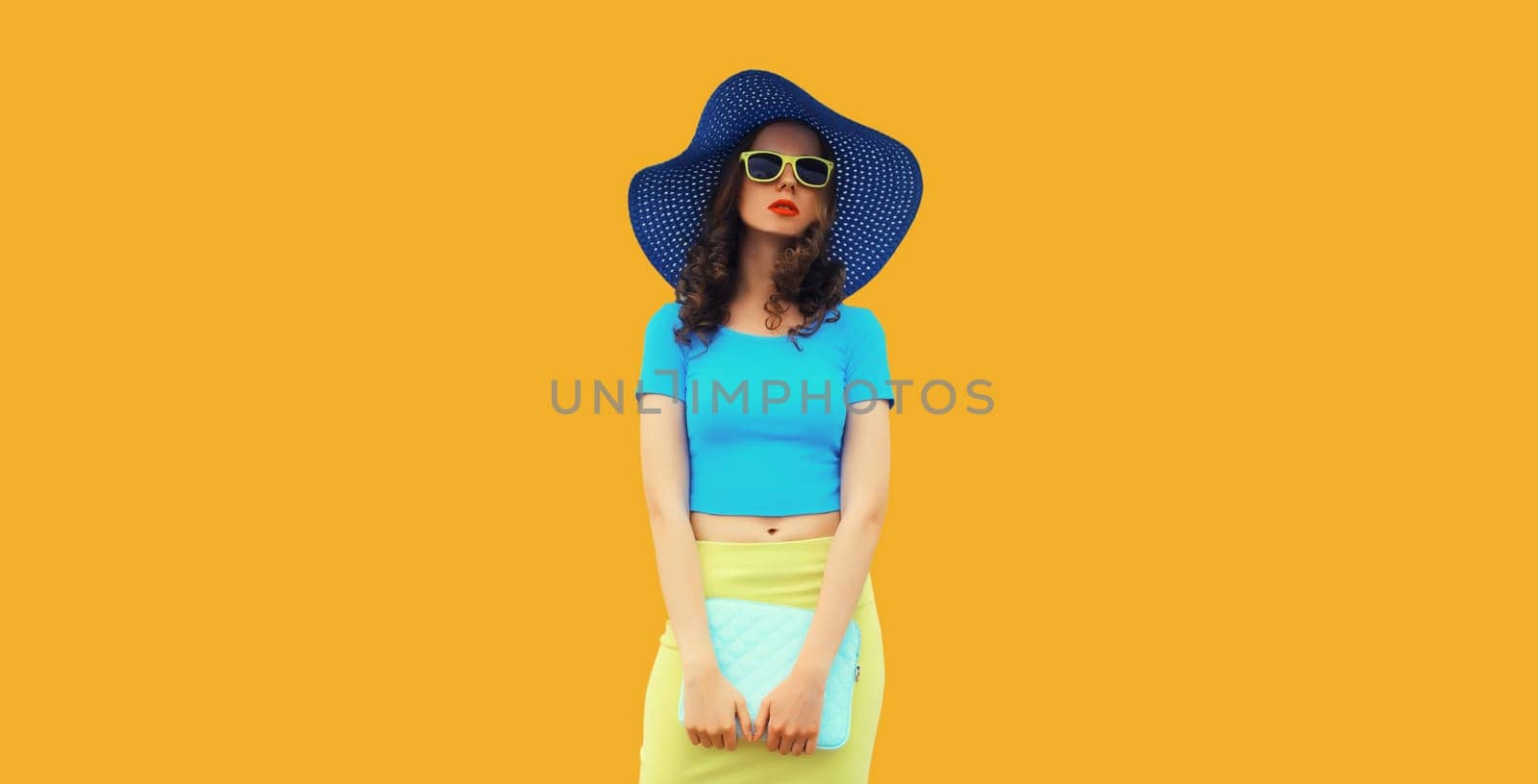 Beautiful young woman model posing with handbag clutch in summer straw hat on yellow background by Rohappy