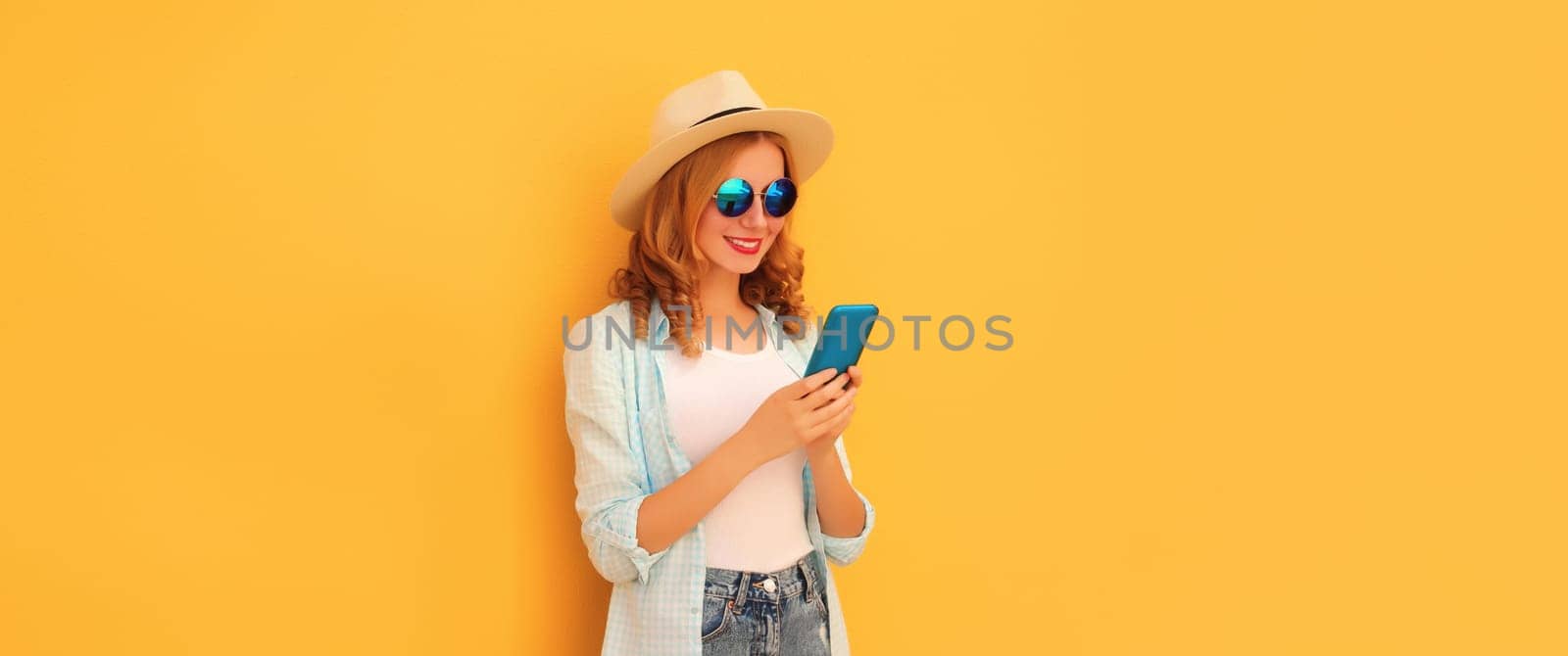 Summer portrait of happy young woman with mobile phone looking at device on yellow background by Rohappy