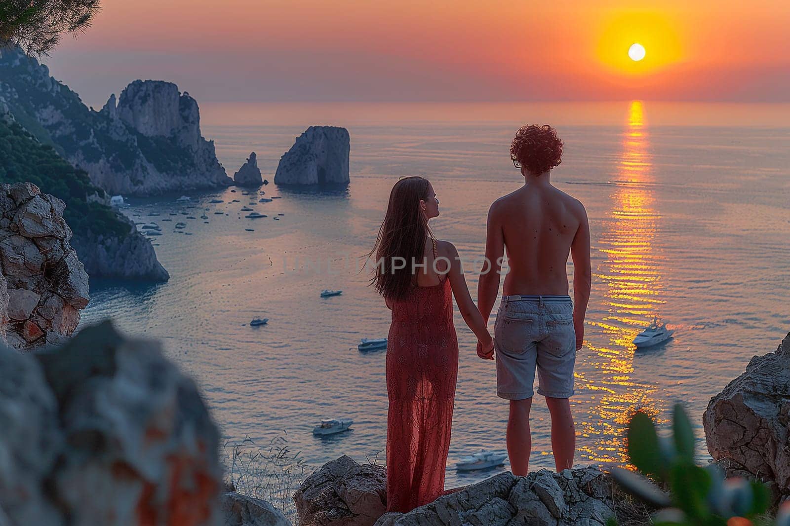 Silhouetted couple watches sunset on Capri, with vibrant skies and golden reflections along the rugged Mediterranean coastline