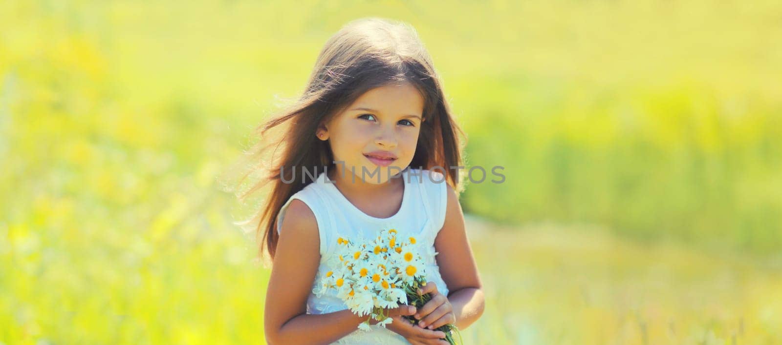 Portrait of cute girl child with wildflowers in sunny summer park
