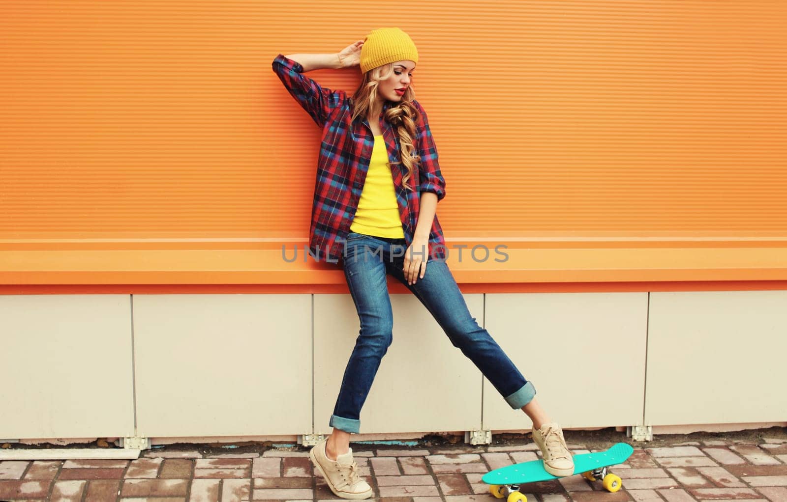 Stylish young blonde woman posing with skateboard in yellow hat, shirt on city street by Rohappy