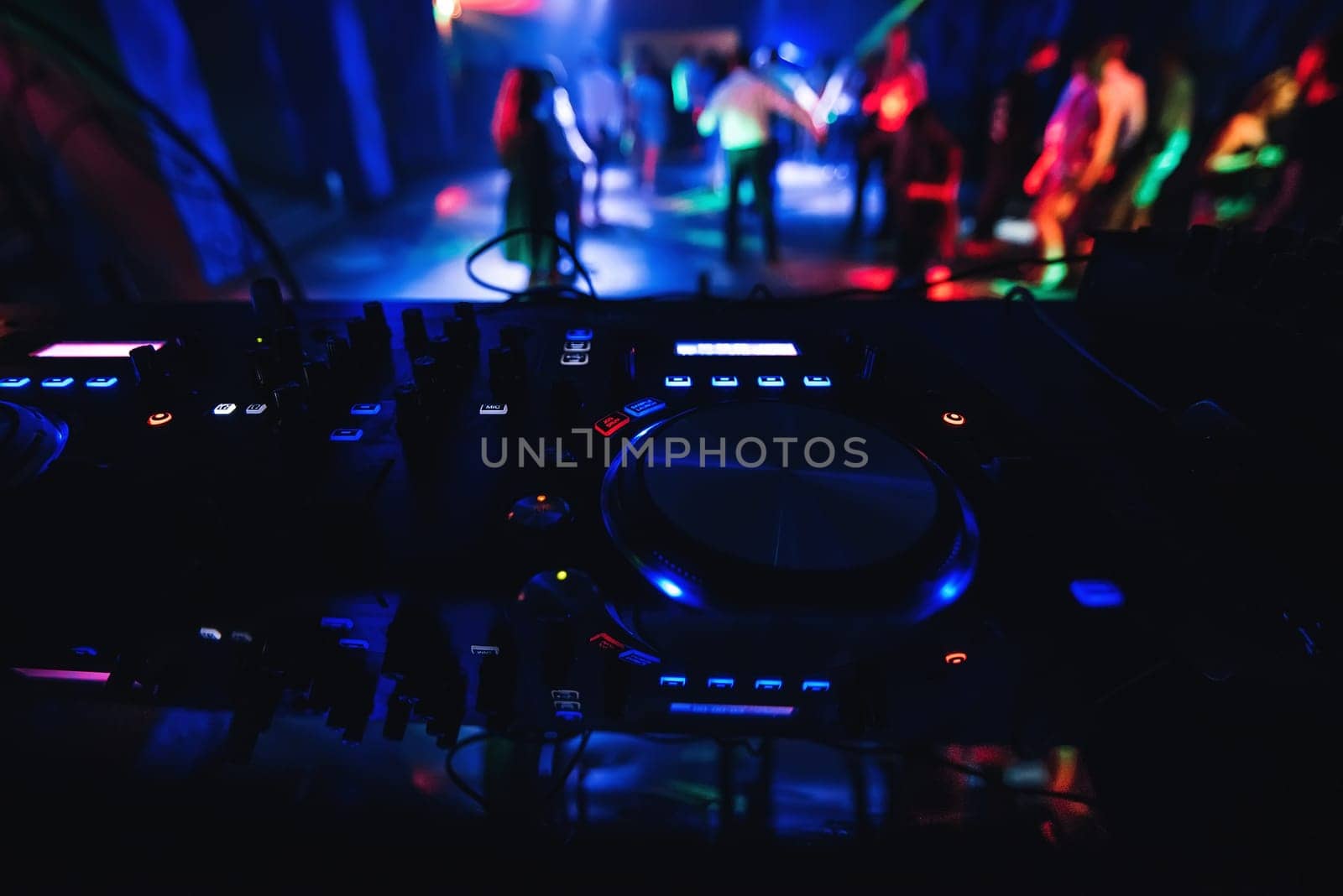 blurred people dancing on the dance floor of nightclub with a DJ mixer in front to control the music