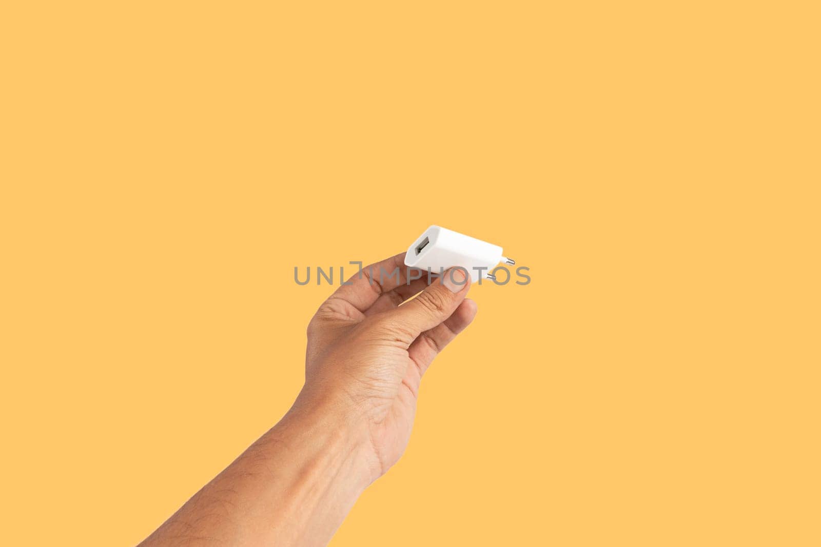 Black male hand holding a USB charger plug isolated on yellow background. High quality photo