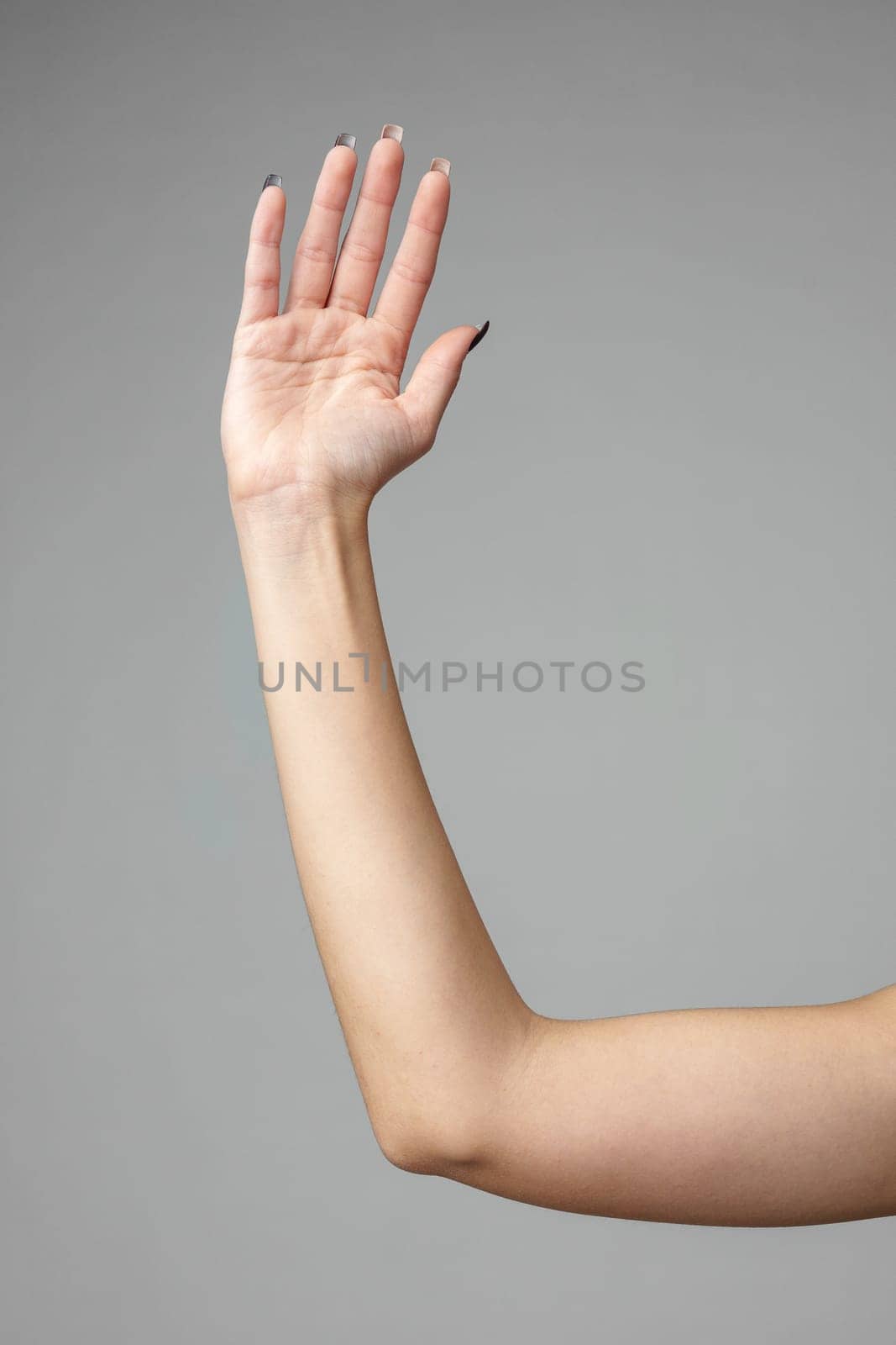 An individuals left hand is raised up against a neutral gray backdrop, displaying an open palm with fingers extended and slightly apart, possibly conveying a sign, signal, or nonverbal communication.