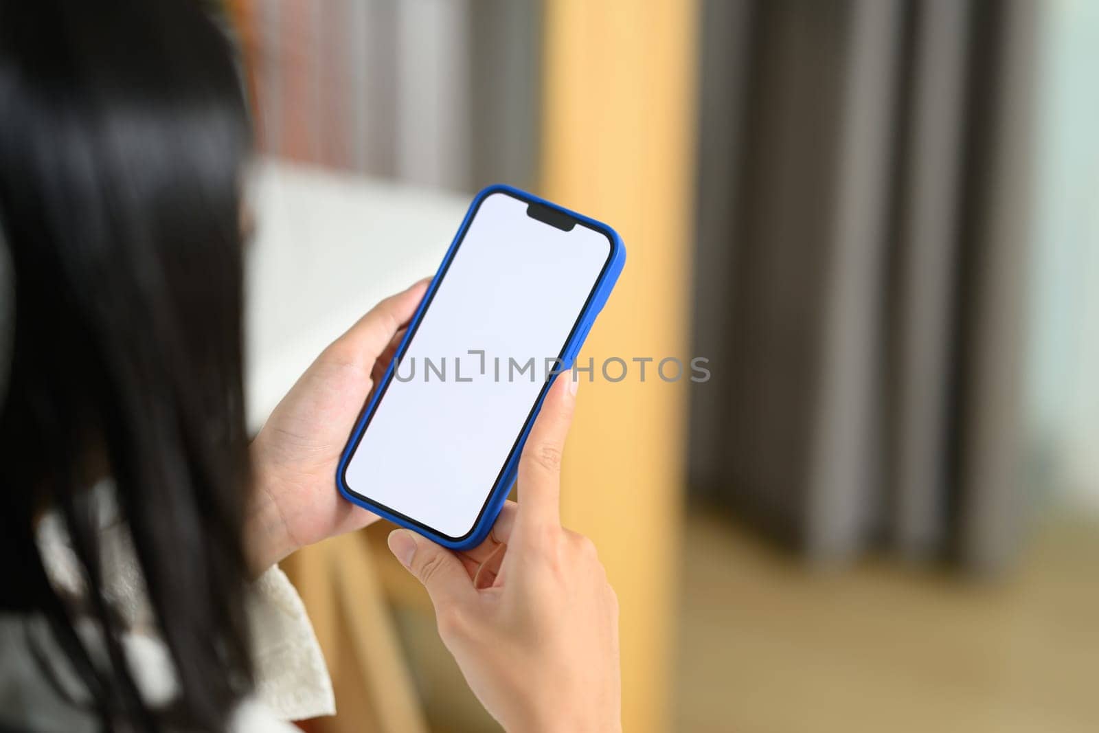 Over shoulder view of woman holding smartphone with blank screen sitting in office by prathanchorruangsak