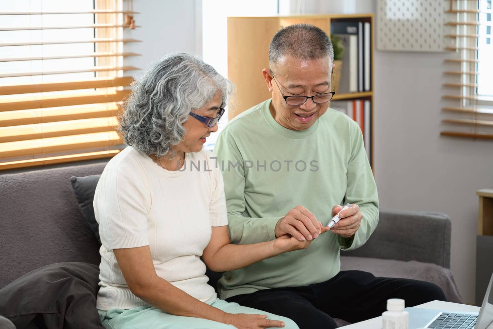Smiling senior man helping his wife checking blood sugar level at home. Health care concept.