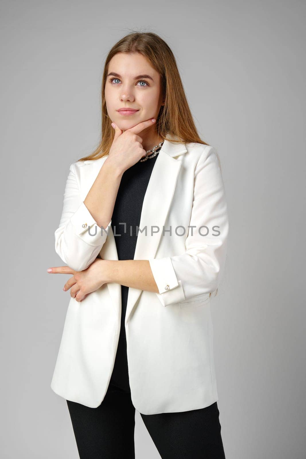 Thoughtful Young Woman in a Stylish White Blazer Posing on gray background by Fabrikasimf