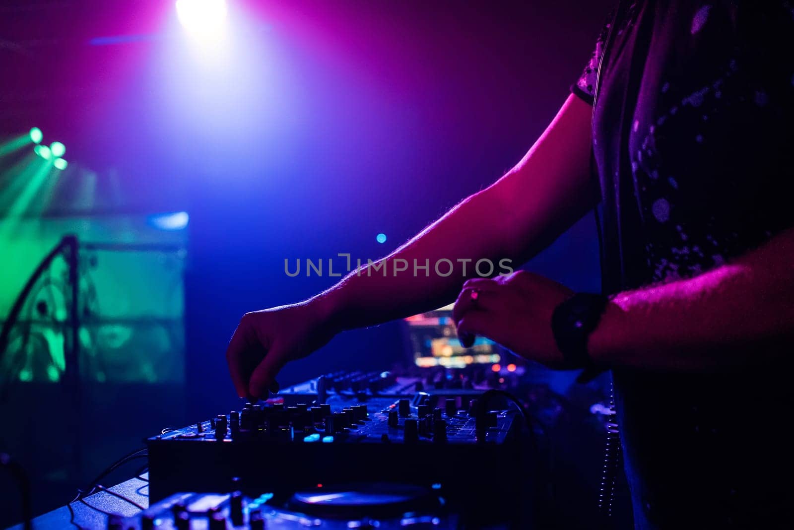DJ in the night club playing at a professional mixer, color-changing spotlights
