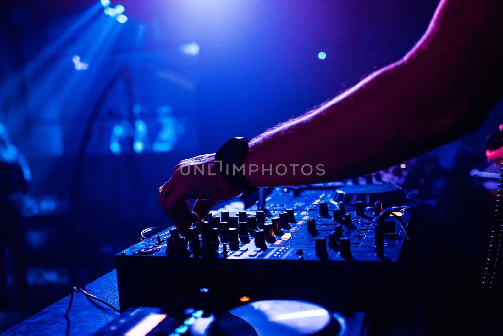 DJ in the night club manages and mixes music on the mixer moving the volume controls