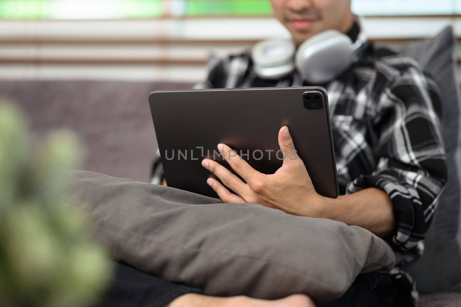 Happy young hipster guy with headphone on neck working remotely from home on digital tablet.