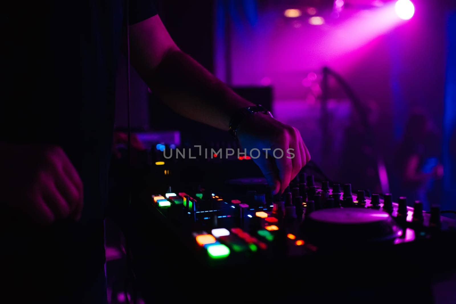 DJ controls the music in the nightclub moving the controllers on the music Board with colorful blurred background