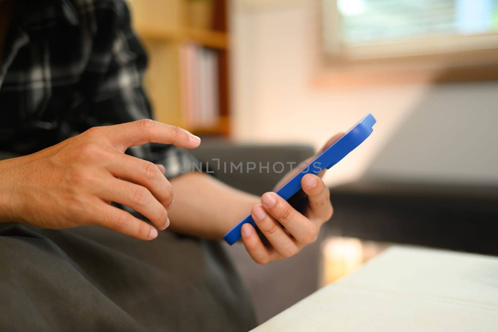Cropped shot man typing messages on mobile phone sitting on sofa in living room by prathanchorruangsak