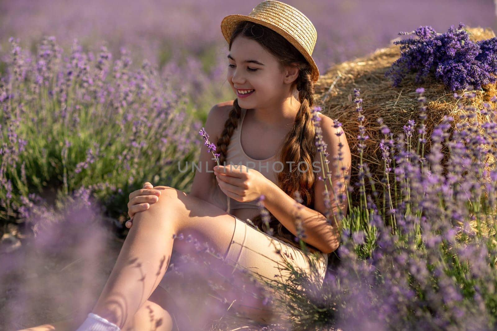 A young girl is sitting in a field of purple flowers, holding a purple flower in her hand. She is smiling and she is enjoying the moment. Concept of happiness and contentment