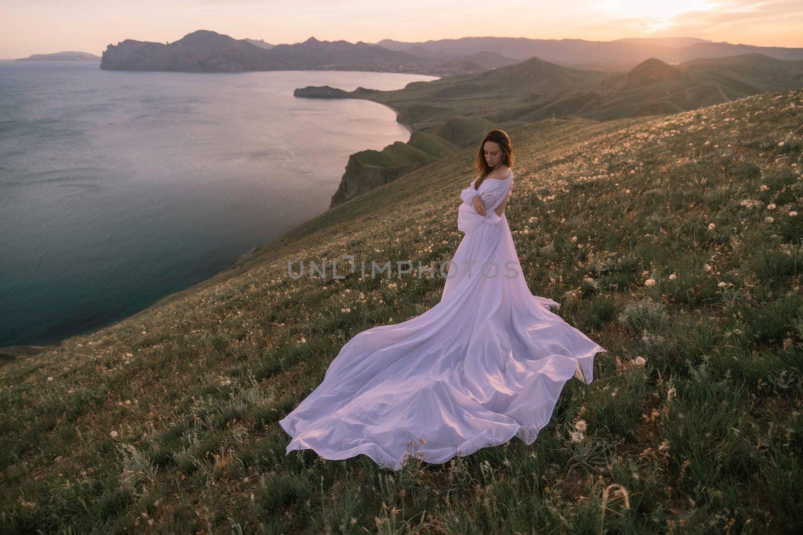 A woman in a long white dress stands on a hill overlooking a body of water by Matiunina