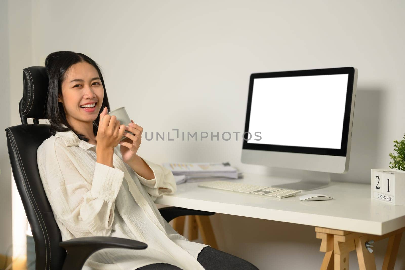 Young businesswoman with mug sitting in front of blank computer screen.
