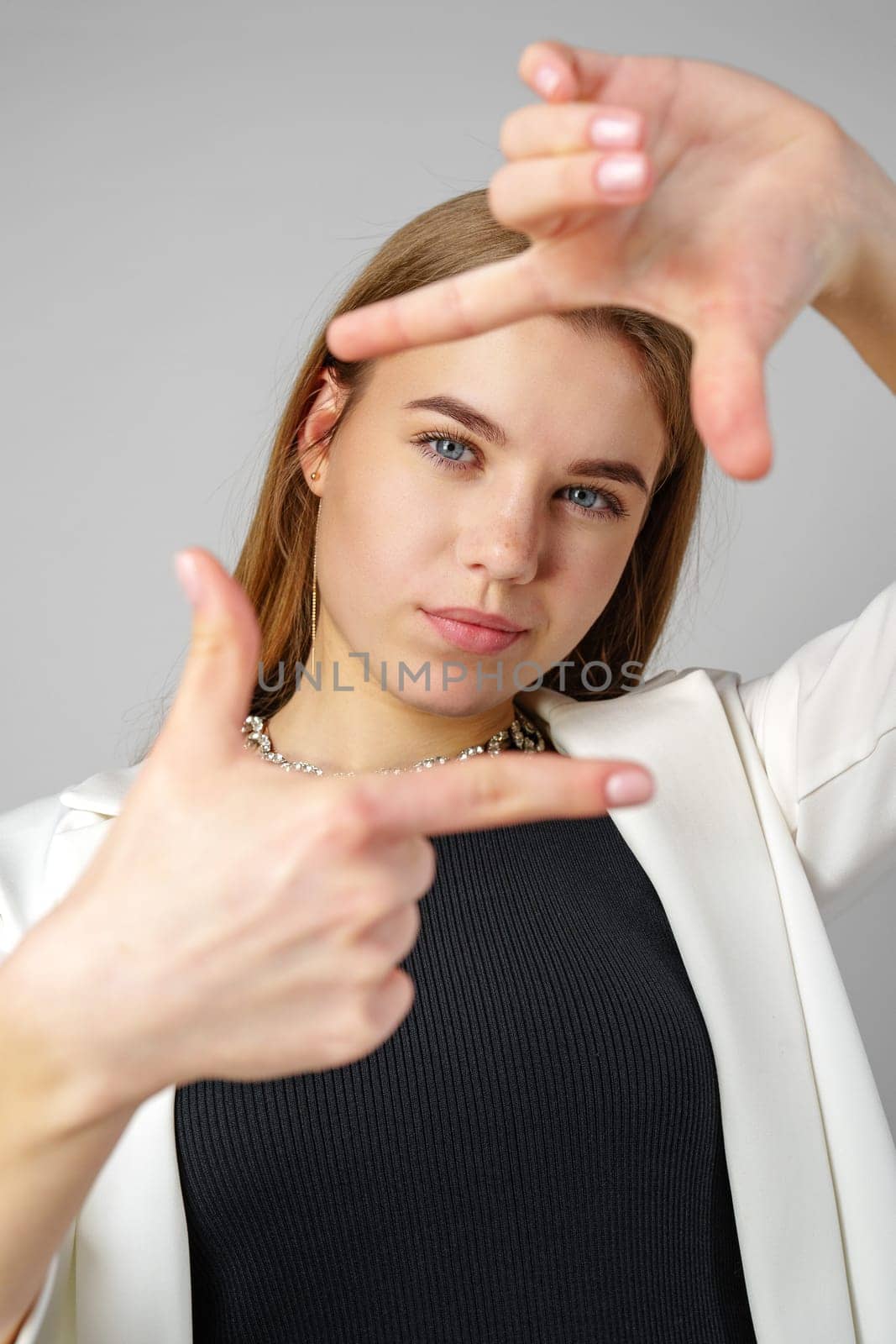 Young Woman Making Frame Gesture With Hands Against a Neutral Background by Fabrikasimf