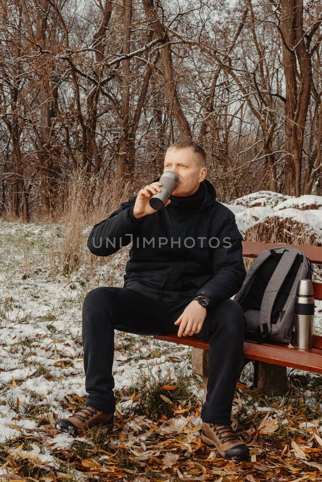 Winter Serenity: 40-Year-Old Man Enjoying Tea on Snow-Covered Bench in Rural Park. Immerse yourself in the tranquil beauty of winter as a 40-year-old man finds solace on a snowy bench in a rural park. by Andrii_Ko