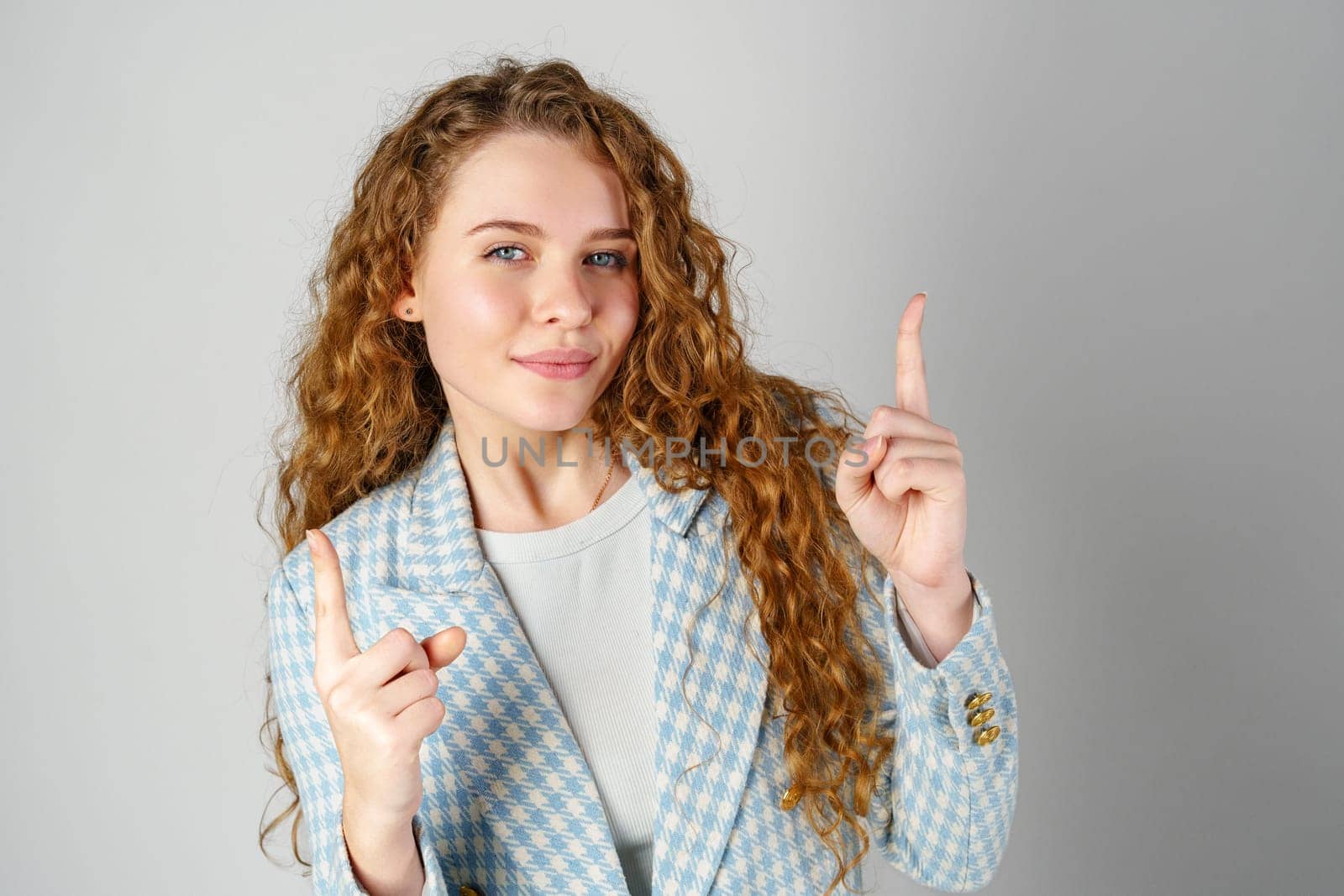 Young Woman With Curly Hair Pointing Upwards in a Studio Setting close up