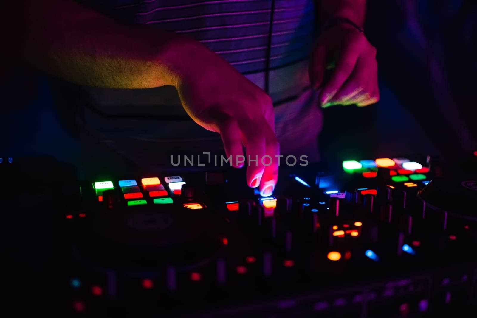 hands on professional DJ mixer with multi-colored glowing buttons mixing music