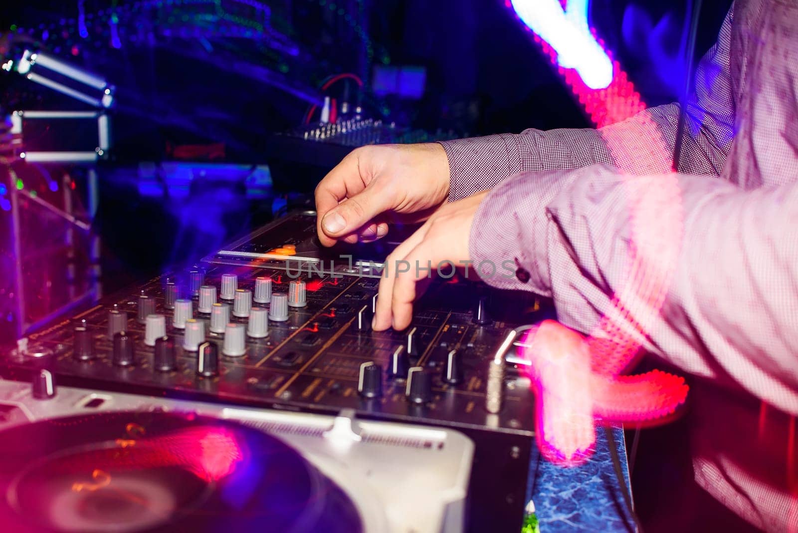 DJ hands mix music on professional mixer in booth at a party in nightclub