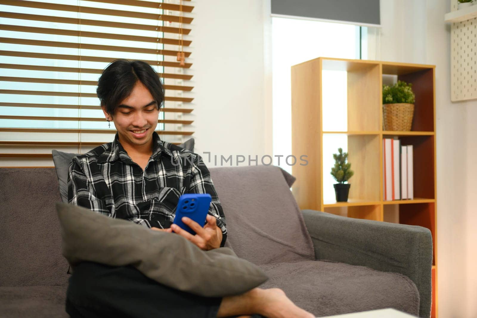 Cheerful young Asian man checking news feed or messaging on his smartphone.