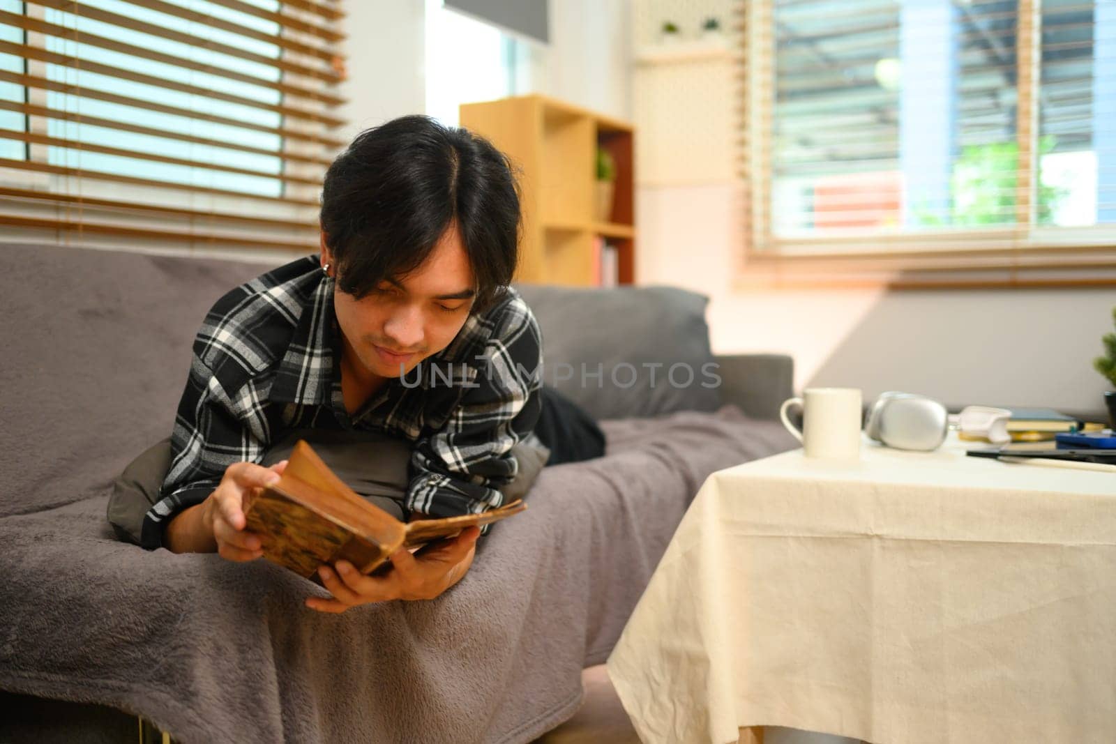 Happy young man lying on couch and reading book. Recreation and leisure activity concepts.