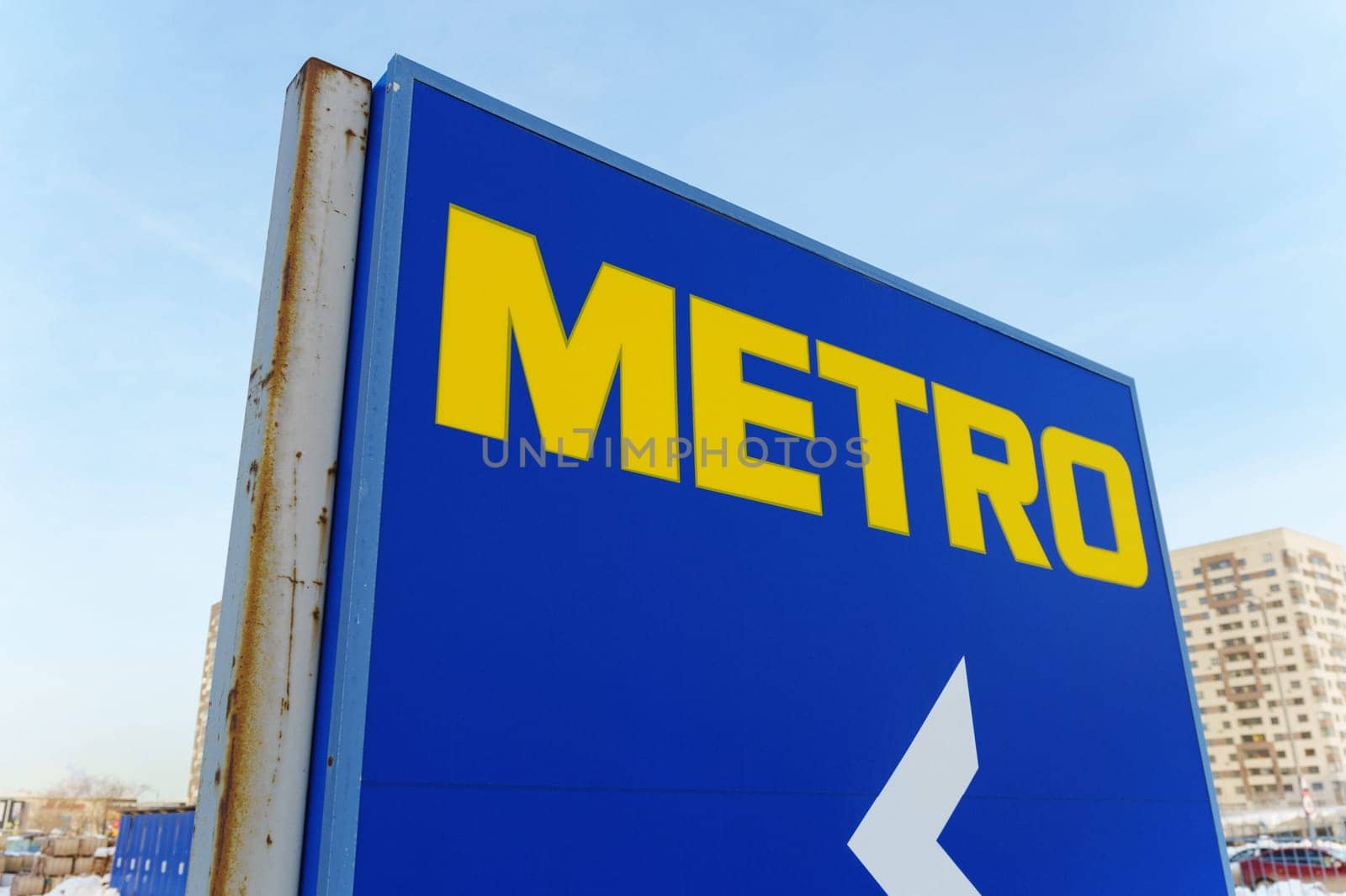 Tyumen, Russia-March 18, 2024: Metro sign glows brightly against the night sky, with the silhouettes of city buildings in the background.