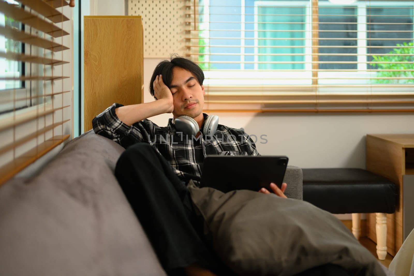 Bored young man freelancer working with digital tablet on couch at home by prathanchorruangsak