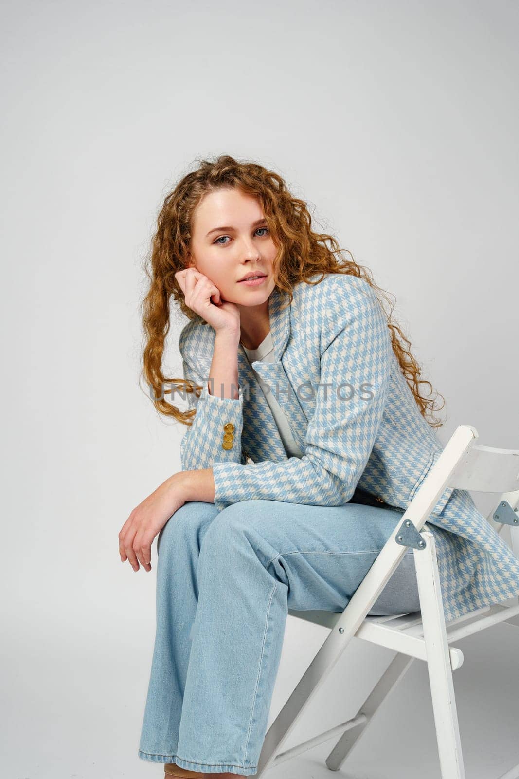Young woman with curly hair sitting on chair in studio close up