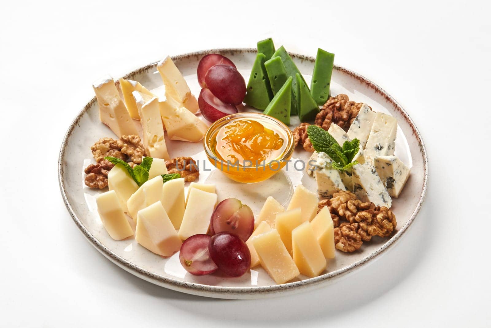 Assorted cheese selection traditionally served with walnuts, grapes and bowl of honey on ceramic plate, on white background. Delicious appetizer