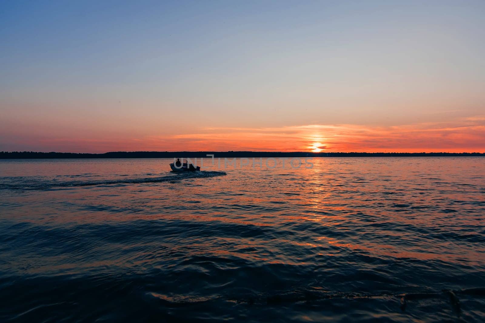 boat floats on the water waves on the background of red and blue sunset with the sun