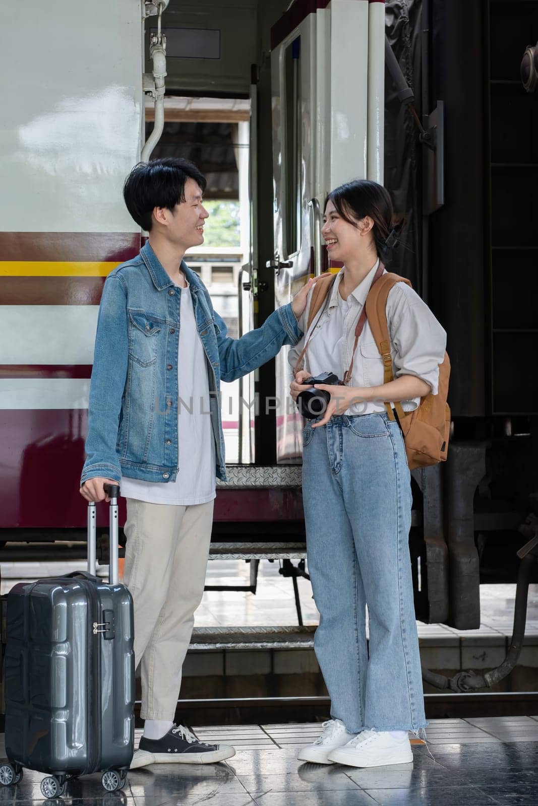 Happy Asian couple holding suitcases and camera preparing to wait for train at train station for vacation trip together. by wichayada