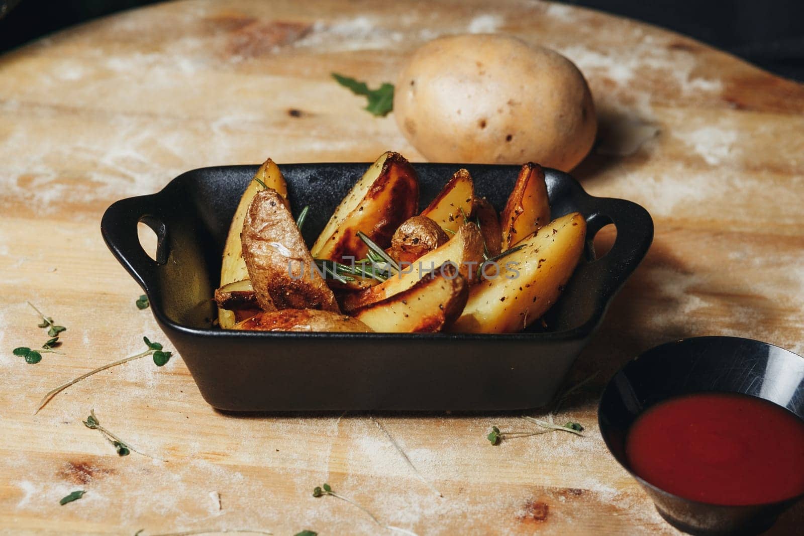 Roasted potatoes glisten in a black bowl on a rustic wooden table, emanating a mouthwatering aroma.