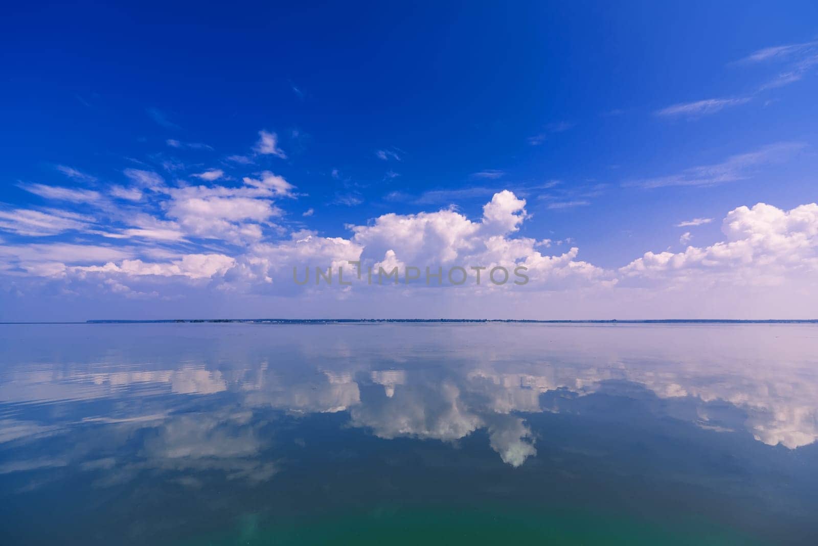blue clear sky with white clouds reflected in the calm water of the sea on a Sunny day