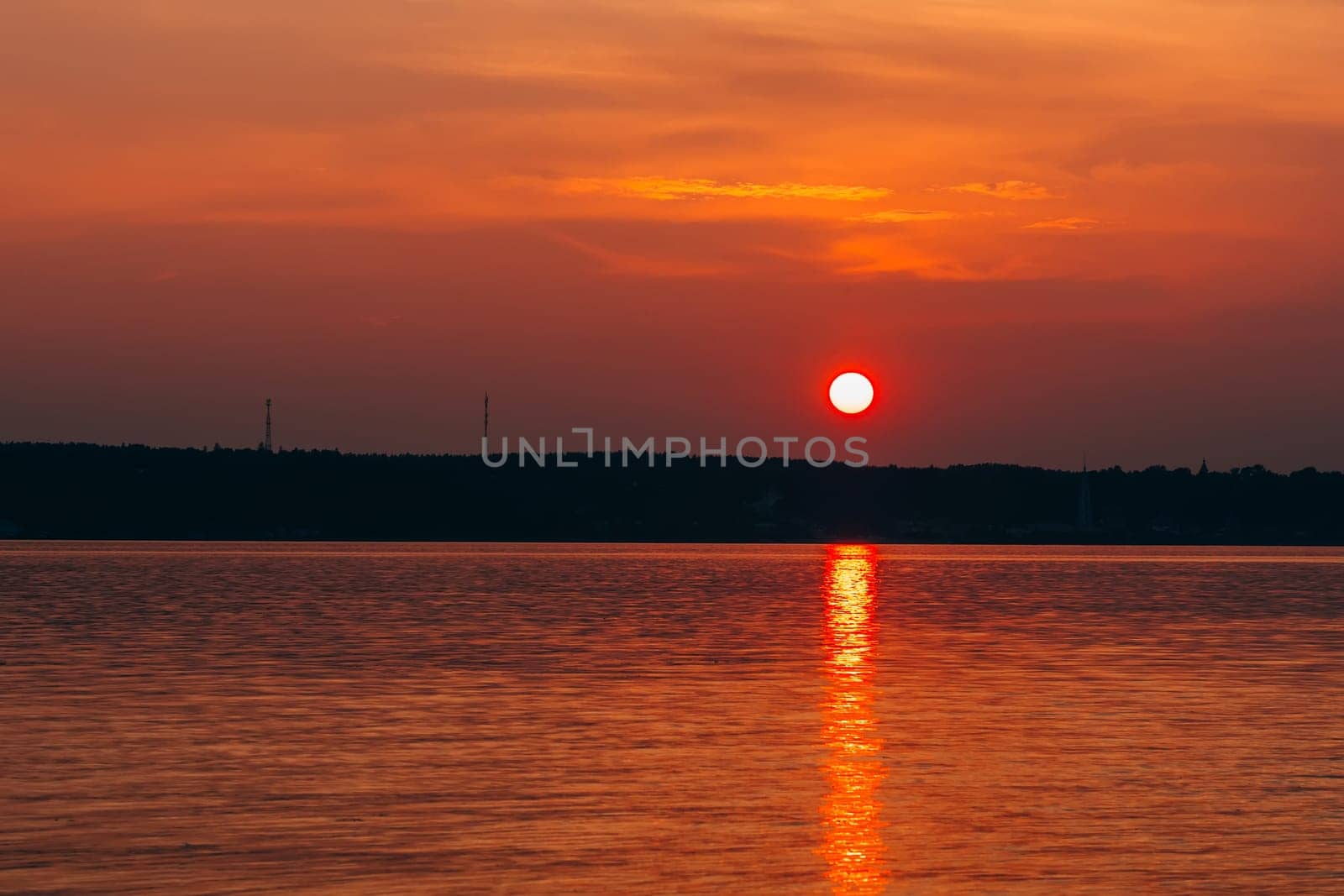 sunset with big red sun over the water of the sea and the silhouette of the shore