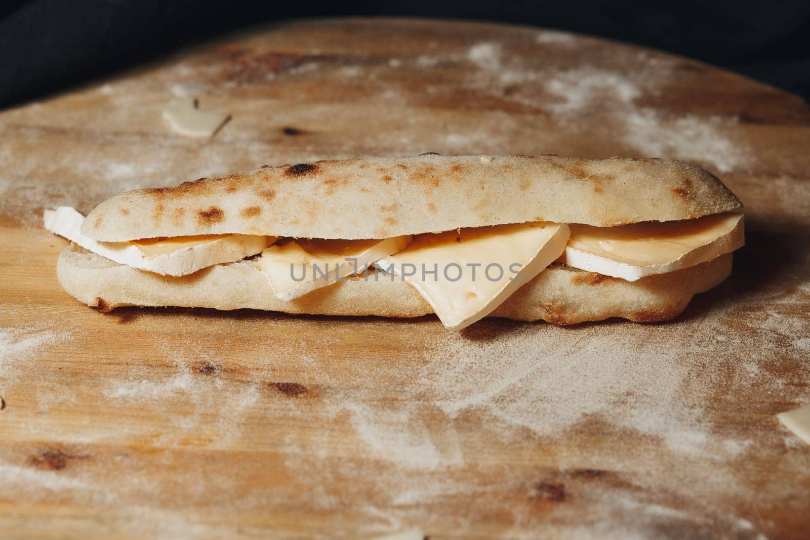 A freshly made sandwich with a generous portion of cheese placed on a rustic wooden cutting board.