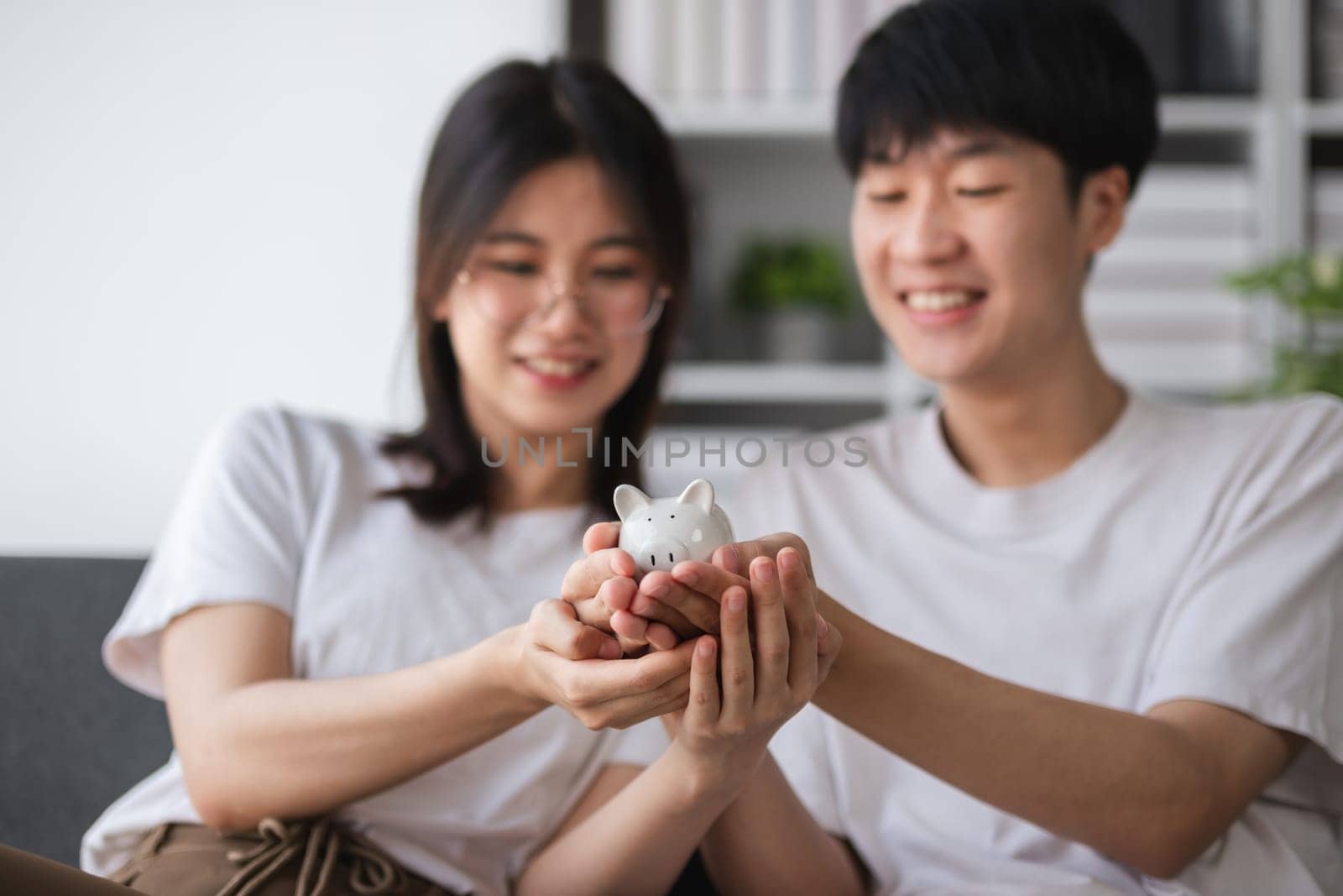 Young couple sitting together on the sofa Holding a pig model, concept of saving money by wichayada