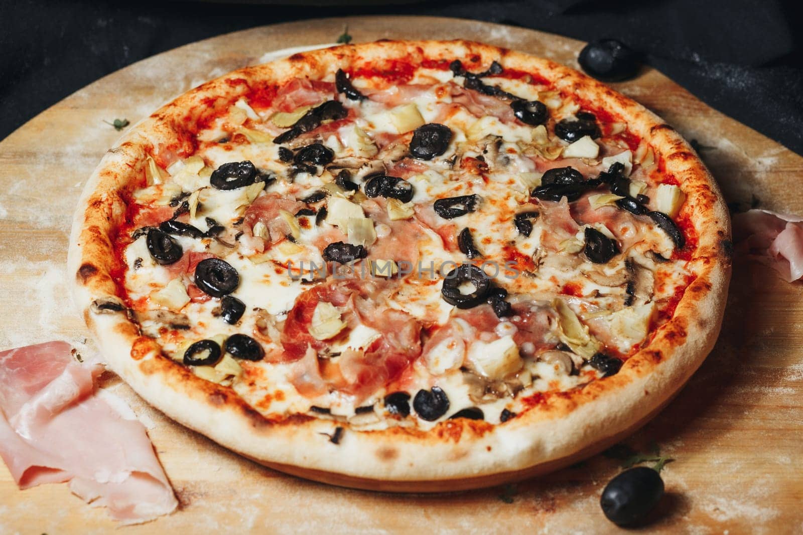 A gourmet pizza with a variety of olives beautifully arranged on a rustic wooden board.