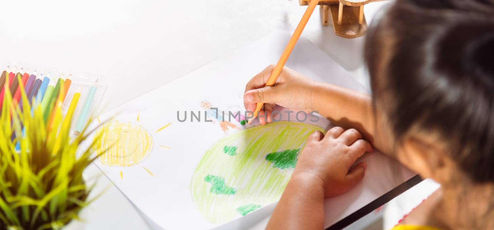 Happy child little girl colorful drawing family standing hold hands on planet earth on paper, Asian cute kid preschooler sit on table smiling she draw picture with pencil at home, earth day concept